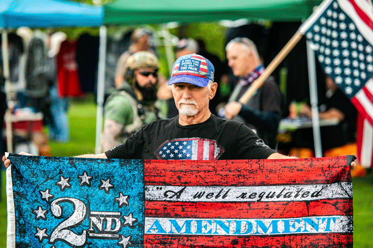 Protester at a Proud Boys rally in Oregon wears a hat and t-shirt featuring the U.S. flag, and carries an American flag emblazoned with a Second Amendment slogan