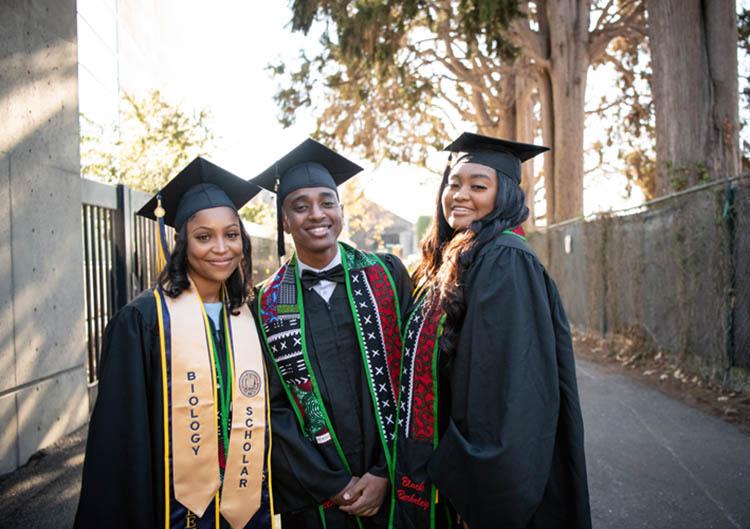 three people in cap and gowns pose for a picture