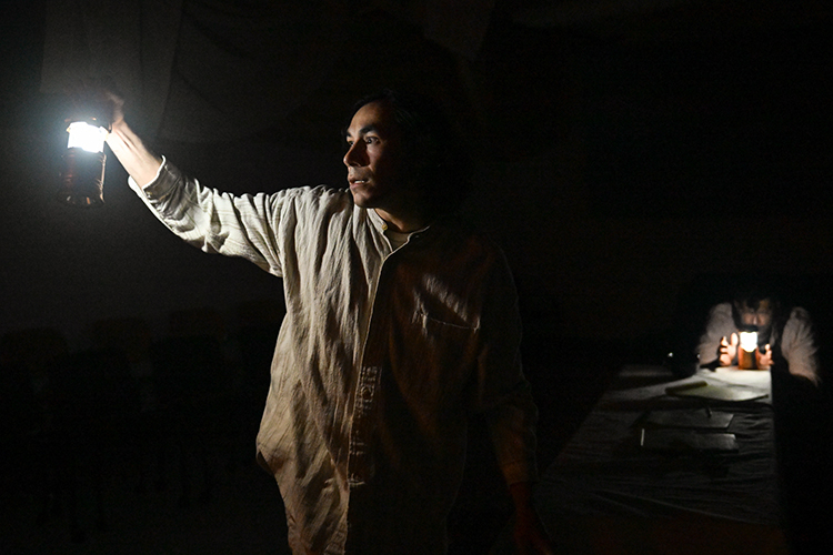 an actor stands in the dark holding a lantern