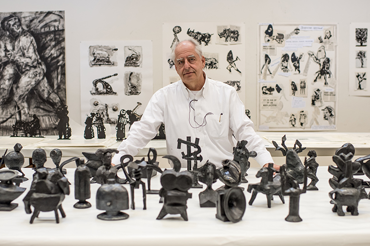 person stands behind a white table with small metal sculptures resting on it