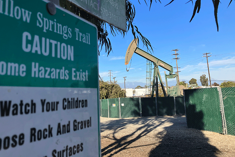 A photo shows an oil rig located in a neighborhood in Los Angeles. In the foreground is a sign for a city park.