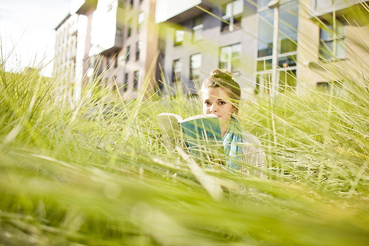 a student sits surrounded by tall grass reading a book
