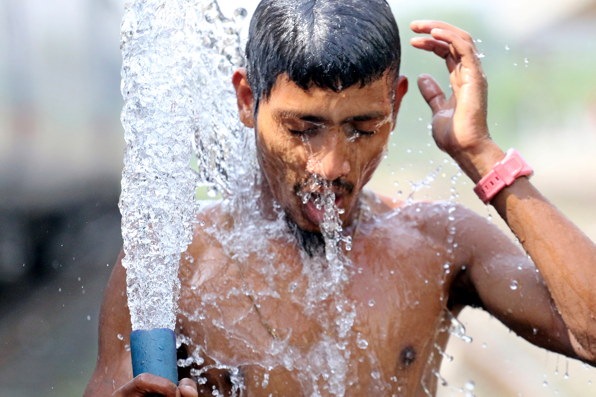 young Indian man spraying water on himself to cool off