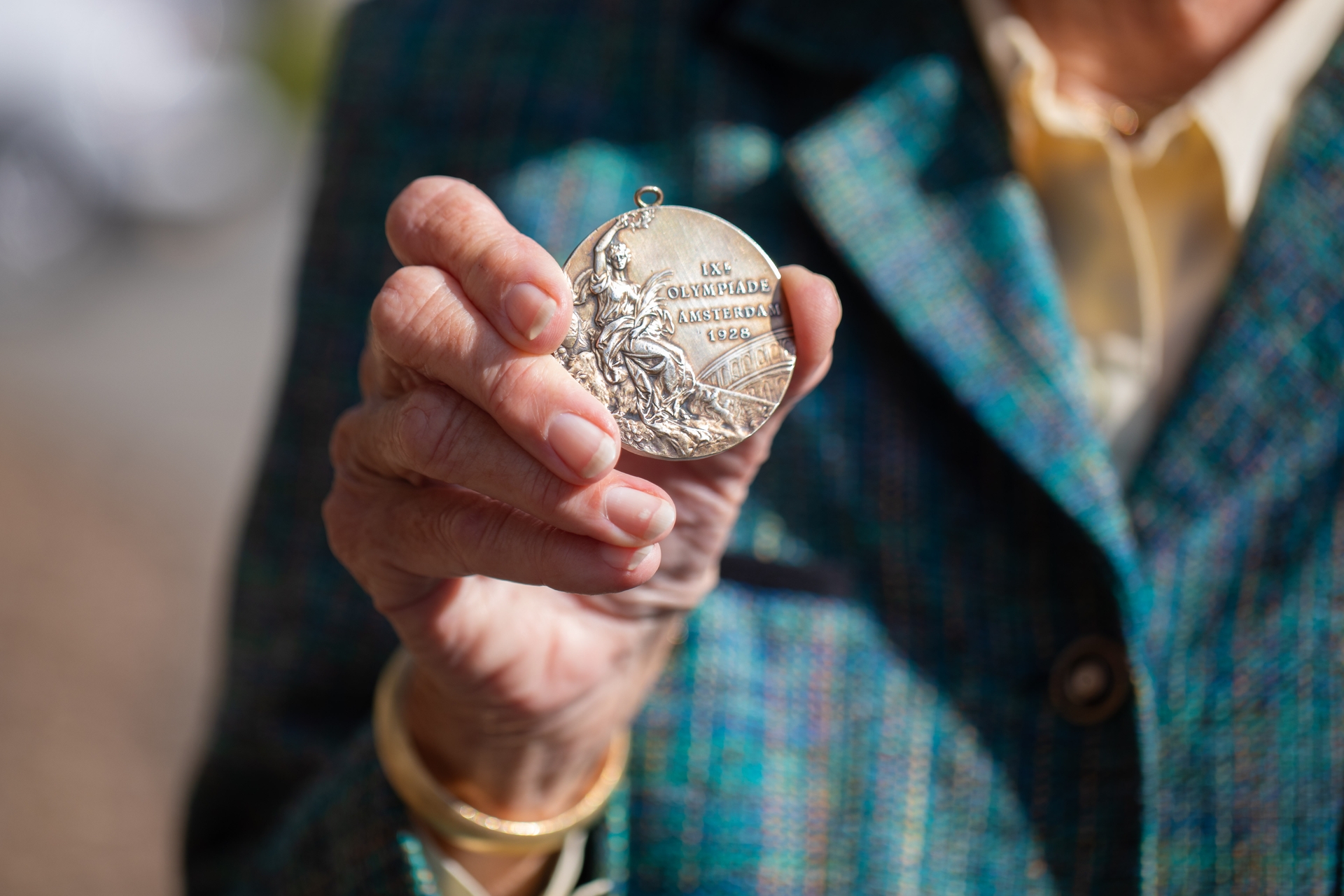 a photo of a hand extended outward and holding an Olympic gold medal from 1928 from Amsterdam