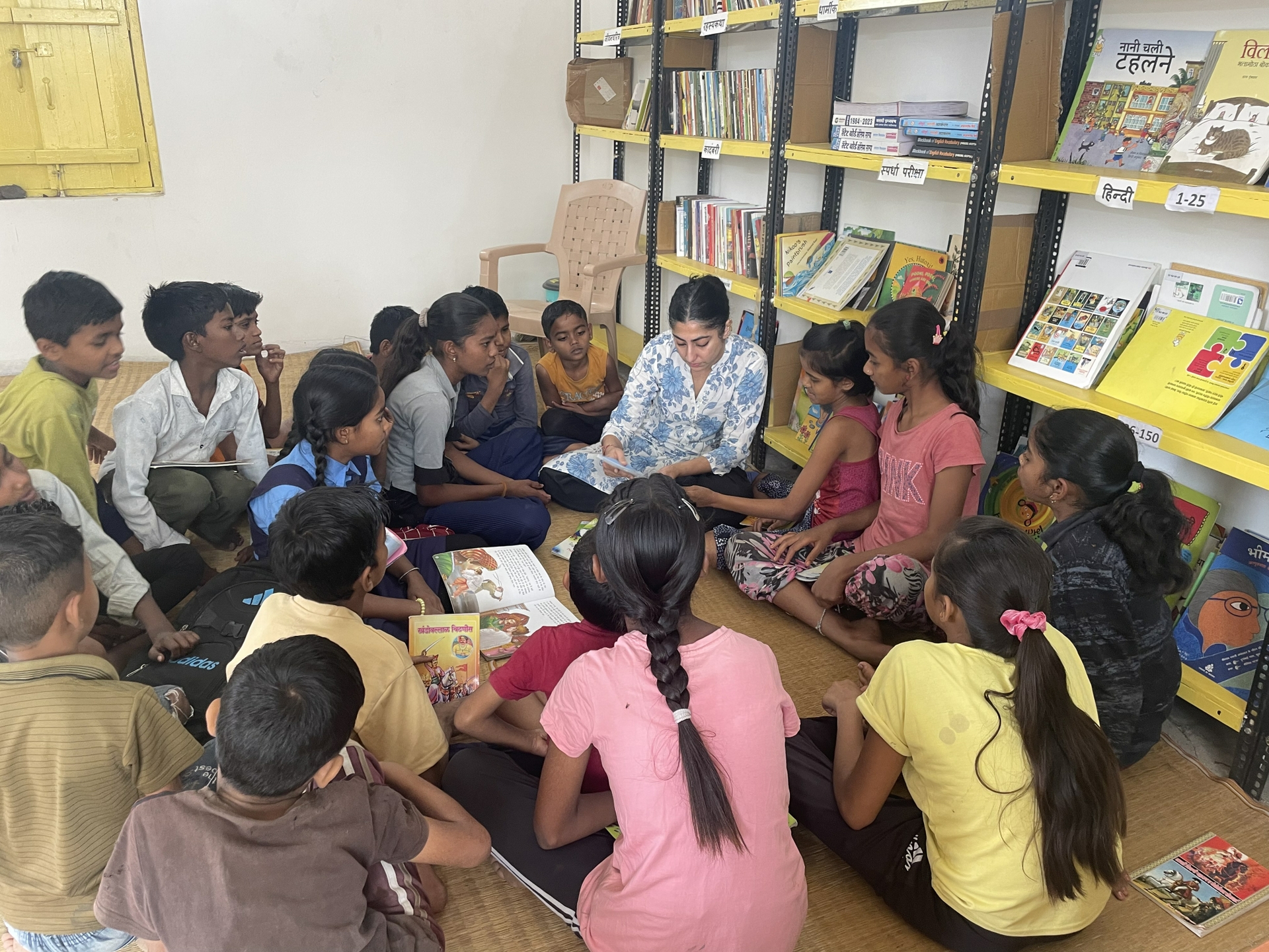 Aarti Sethi is surrounded by about a dozen kids, sitting around her crosslegged and listening to her read. They're gathered in front of a library bookshelf.