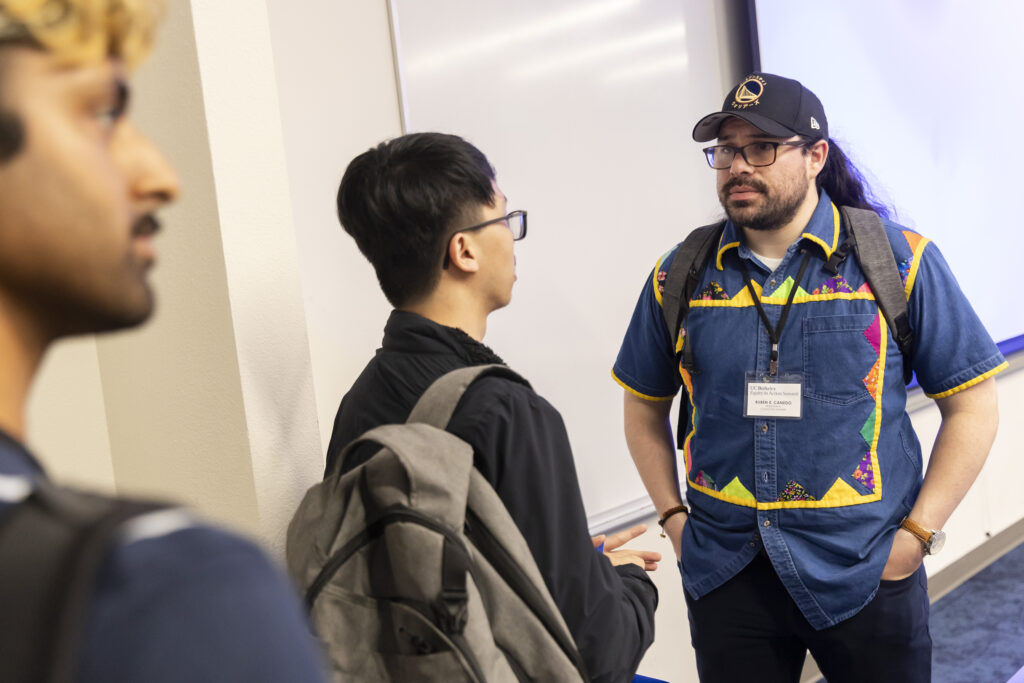 A man who just gave a presentation at a UC Berkeley summit talks with a student carrying a backpack who was waiting to ask him questions. Another student is standing behind that student.