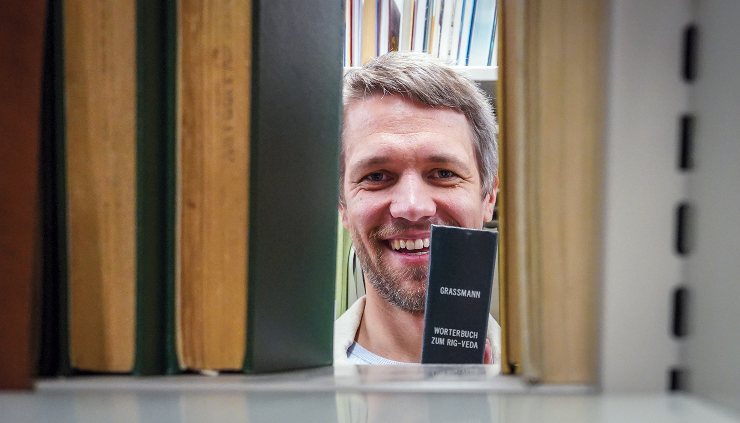UC Berkeley linguist Gašper Beguš peers through a row of books in a library