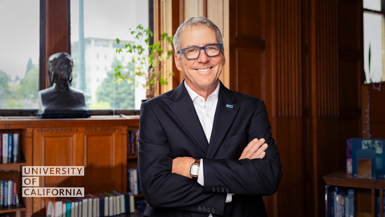 UC President James B. Milliken stands with arms crossed in a still photo.