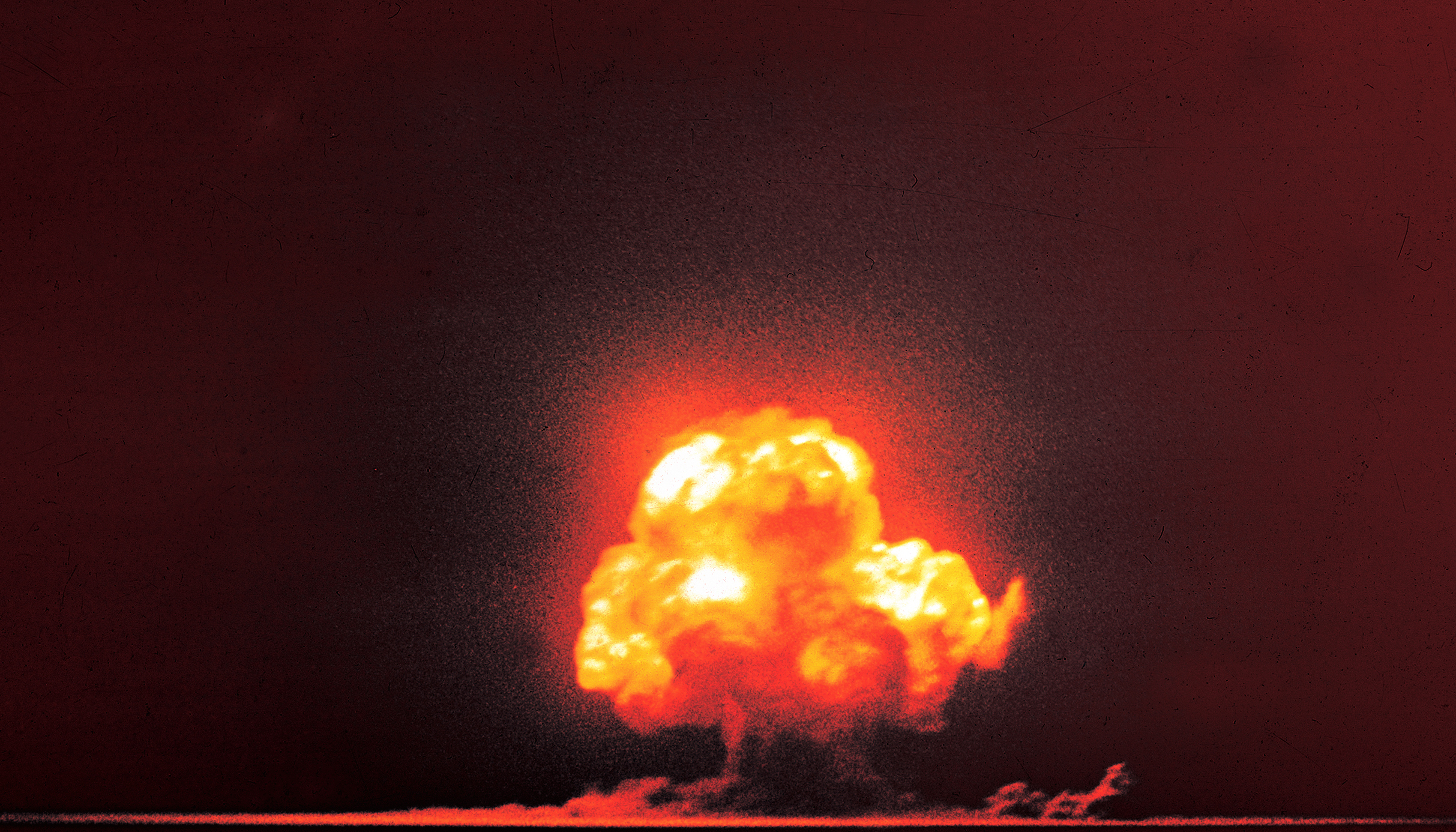 A slightly blurred and radiant color image of the first nuclear test explosion with a cloud of fire in the darkness, seen from a distance.